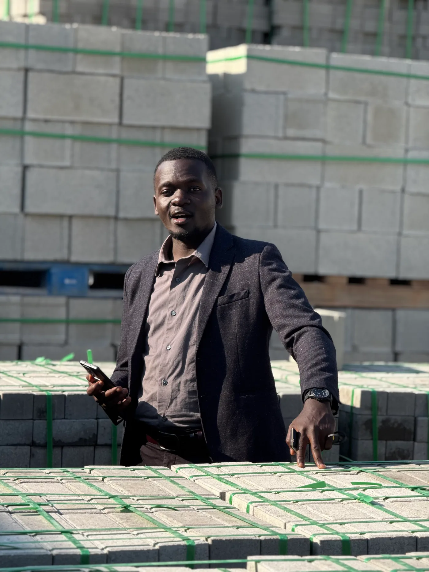 Matthew Muwanguzi Mugagga, director, standing in the yard with stacked product behind him